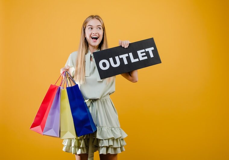 Tjej med shoppingpåsar hållandes en OUTLET-skylt